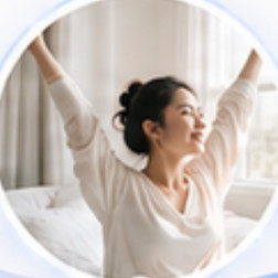 A woman sitting up in bed, stretching her arms above her head beside a bright window